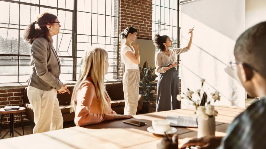 A group of coworkers brainstorming together at a white board in a modern office setting.