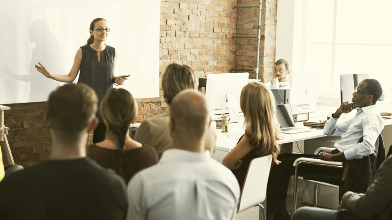 A facilitator stands at the front of a group of people who are listening and engaged